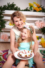 Nice mom and beautiful blonde daughter in room durin spring photo shoot before easter with festive decorated eggs. Happy girl and woman having rest and joy together