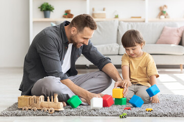 Family leisure. Cute boy playing colorful blocks with happy daddy, spending weekend together, sitting on floor at home