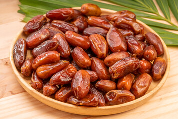Dried date palm fruit on a wooden plate, date palm fruit with leaf on wooden background