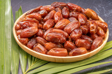 Dried date palm fruit on a wooden plate, date palm fruit with leaf on wooden background