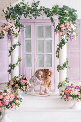 girl is sitting on a wooden rocking horse on the veranda of a house decorated with flowers. A child...