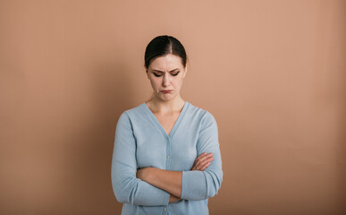 Obraz premium a disgruntled brunette woman with glasses in a blue jumper stands and lowered her eyes down on a beige background with a place for text