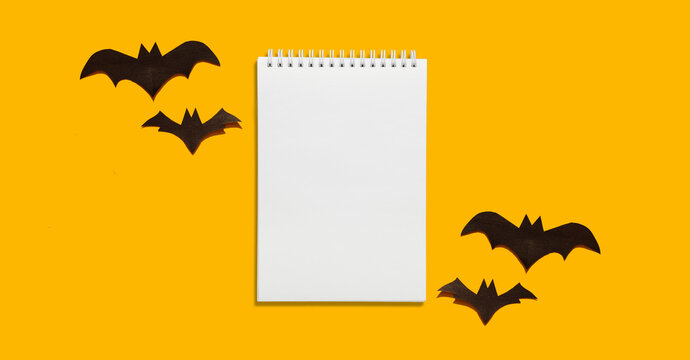 Halloween set decorations with bat and mock up empty notebook list on yellow background. Holiday party composition, minimal card, spooky concept. flat lay, copy space, top view, place for text