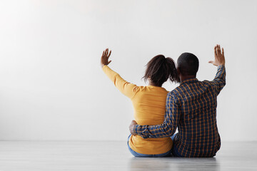 Millennial black family planning interior with raised hands up, sit on floor on gray wall...