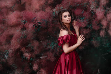 Beautiful woman in red dress walking in the garden full of roses.