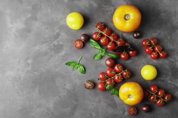 Fototapeta na wymiar Composition of ripe fresh tomatoes of different varieties, mini bell peppers, spices, rammarine, thyme, basil, chilli pepper, on a concrete textured background with space for text.