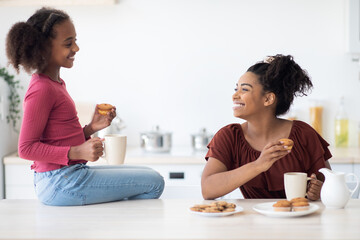 Cheerful african american mom and daughter drinking tea with cupcakes
