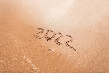 2022 years and 2021 washed away by a wave on the sand. New year 2022 concept. Summer vacation and travel by sea