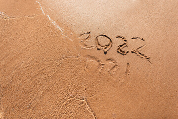 Message Year 2021 replaced by 2022 written on beach sand background. Good bye 2021 hello to 2022. Happy New Year coming concept