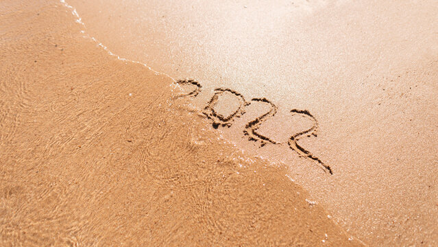 2022 figures are drawn on the sand on the beach by the sea. New Year's Eve 2022 concept. Summer holidays. 2022 wash away with a wave