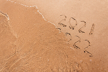 New year 2021 and 2022 is drawn on the sand on the beach near the sea with a wave, top view. Summer vacation and rest, new season. Figures 2021 and 2022 on the sand. Concept idea