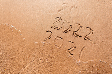Message Year 2021 replaced by 2022 written on beach sand background. Good bye 2021 hello to 2022...