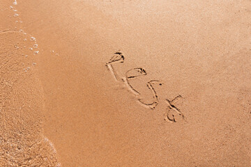 The word Rest is written on the yellow sand on the beach with a wave near the sea, top view. Summer vacation concept