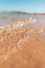 Close-up of water near the sea with yellow sand and blue sky. Nice ocean view. Macro nature water. Summer rest, vacation and travel