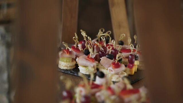 Appetizing fresh snacks of baguette, ham, red bell peppers, olives and grapes with skewers lie on black tray. Fourchette banquet with appetizers, food on wooden rack.