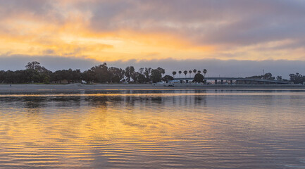 Sunrise on the Mission Bay in California shows boats with their reflections in the orange of the rising sun. Sailors ready to take their sailboats on an adventure