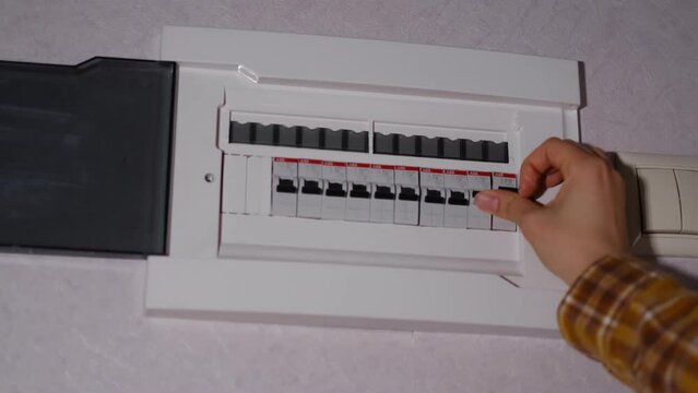electrical panel in the apartment. Fuse box. Hand switching power switch on a fusebox. Close up of electrician checking fuse box knob
