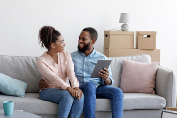 Obraz premium Happy young black male and female relax on couch using tablet for online buying furniture