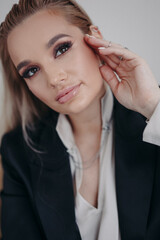 Obraz premium Busy woman, blonde with long hair in a black suit posing in a room on a gray background