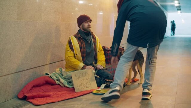 A stranger gives alms to a vagrant man with a dog