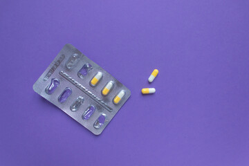 An almost empty silver blister with vitamins in white-yellow capsules on a very peri background....