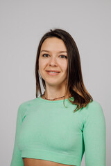 Beautiful woman posing in studio. Portrait of happy young brunette in green top for yoga or fitness, she stands on gray isolated background and smiles.