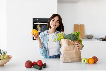 Healthy diet and lifestyle. Happy young lady unpacking paper bag with fresh organic vegetables, greens and fruits