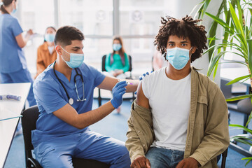 Blck Guy Receiving Coronavirus Vaccine Injection Sitting With Doctor Indoor