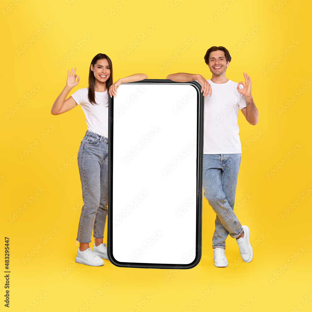 Poster couple showing white empty smartphone screen and gesturing ok