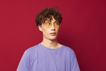 Fototapeta na wymiar Young curly-haired man in yellow glasses purple t-shirt emotions red background