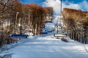Empty chairs at station of ski-lift chair at resort Snowland Valca in winter season.