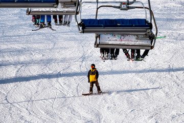 People sitting on chairlift and snowboarder on slope at mountain resort.