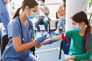 Girl wearing face mask and medical tourniquet giving blood sample - obrazy, fototapety, plakaty