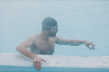Fit swimmer male training swim in open winter swimming pool with fog. Geothermal outdoor spa health concept,