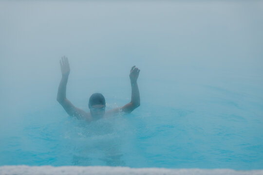 Fit swimmer male training swim in open winter swimming pool with fog. Geothermal outdoor spa health concept,