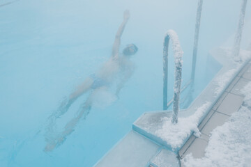 Fit swimmer male training swim in open winter swimming pool with fog. Geothermal outdoor spa health concept,