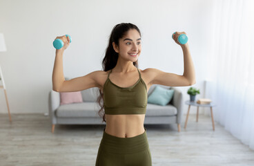 Fototapeta na wymiar Portrait of beautiful young Indian woman keeping fit, training with dumbbells at home. Staying healthy during lockdown