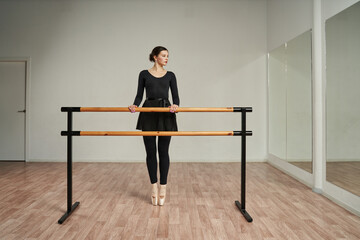the ballerina stands on her toes in pointe shoes in front of the mirror and holds her hands on the ballet loom.