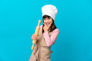 Little girl holding a rolling pin isolated on blue background happy and smiling