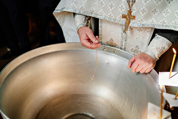 Fototapeta na wymiar a cross on a gold chain is dipped in water for baptism in the font of the church. 