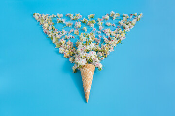 Sweet crispy waffle cup with chestnut flower on blue background. The petals are scattered in the shape of a wineglass