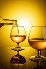 glass of cognac on the table on a yellow golden background. bottles of cognac