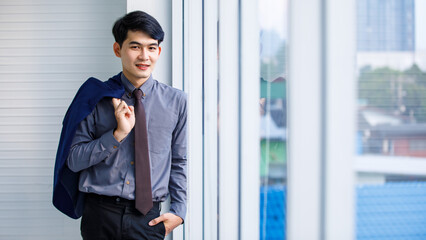 Portrait tudio shot of millennial Asian confident professional successful male manager businessman entrepreneur in formal outfit standing smiling holding suit jacket standing near skyscraper office 