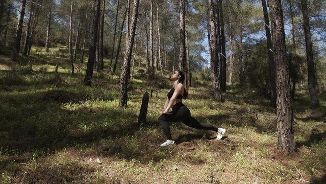 Girl in black clothes warming up with lunges in the forest