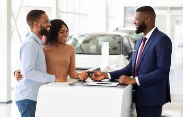 Purchasing Car. Happy Black Couple Key From Manager In Dealership Center