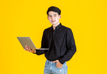 Portrait closeup studio shot of Asian man happy male businessman model in casual outfit standing holding laptop computer for advertising on yellow background