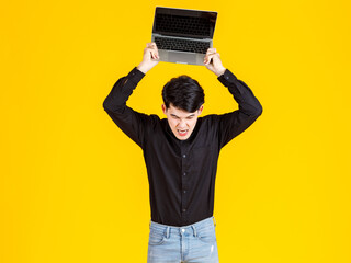 Studio shot of millennial Asian angry mad crazy male businessman employee model in casual outfit standing holding throwing black blank screen laptop computer for advertising text on yellow background