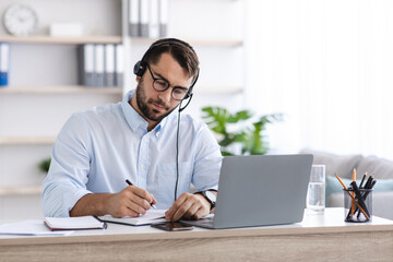 Fototapeta premium Busy middle aged european man with beard in glasses, headphones working at laptop