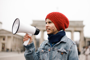 Teenage girl with a woman symbol painted on her face speaking on a megaphone at a demonstration
