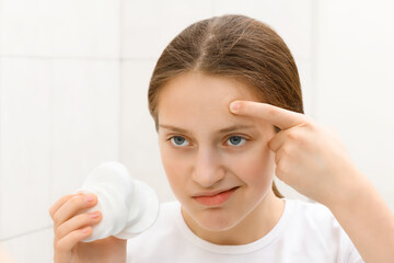 face of a teenage girl, she looks at herself in the mirror and takes care of her skin, does...